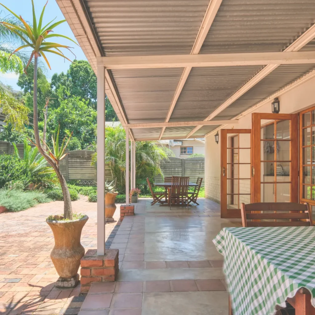 Σταθερό στέγαστρο σε βεράντα σπιτιού με πλακάκια, που προσφέρει αποτελεσματική και μόνιμη αρχιτεκτονική σκίαση.