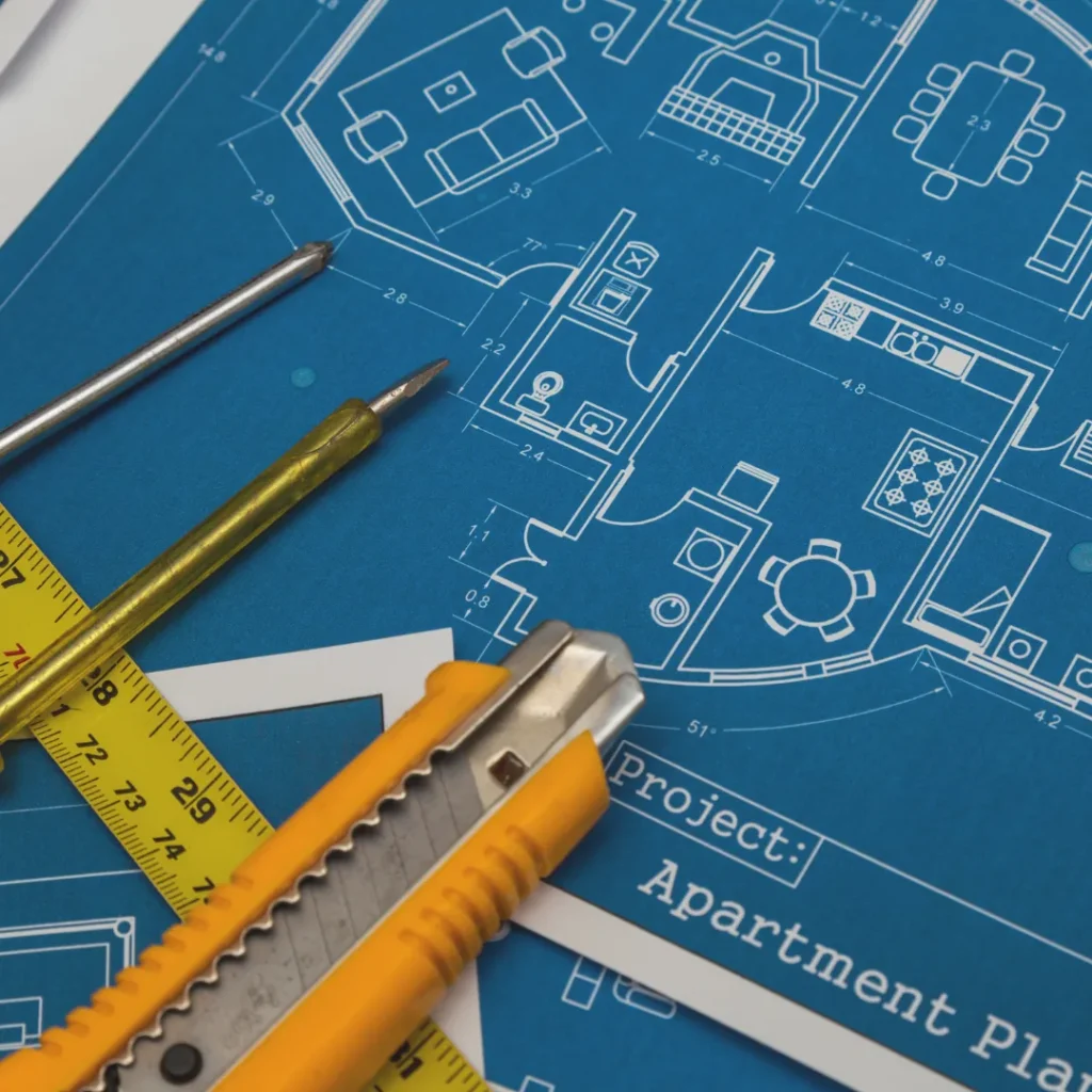 Εργαλεία μέτρησης και κοπίδι πάνω σε αρχιτεκτονικά σχέδια για ακριβή προϋπολογισμό