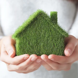 Γυναικεία χέρια κρατούν προστατευτικά ένα σπίτι φτιαγμένο από φυσικό γρασίδι