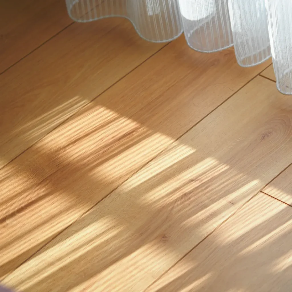 Φυσικό φως ήλιου που πέφτει σε ξύλινο δάπεδο δίπλα σε παράθυρο, αντιπροσωπεύοντας τη ζεστασιά και τον βιοκλιματικό σχεδιασμό.